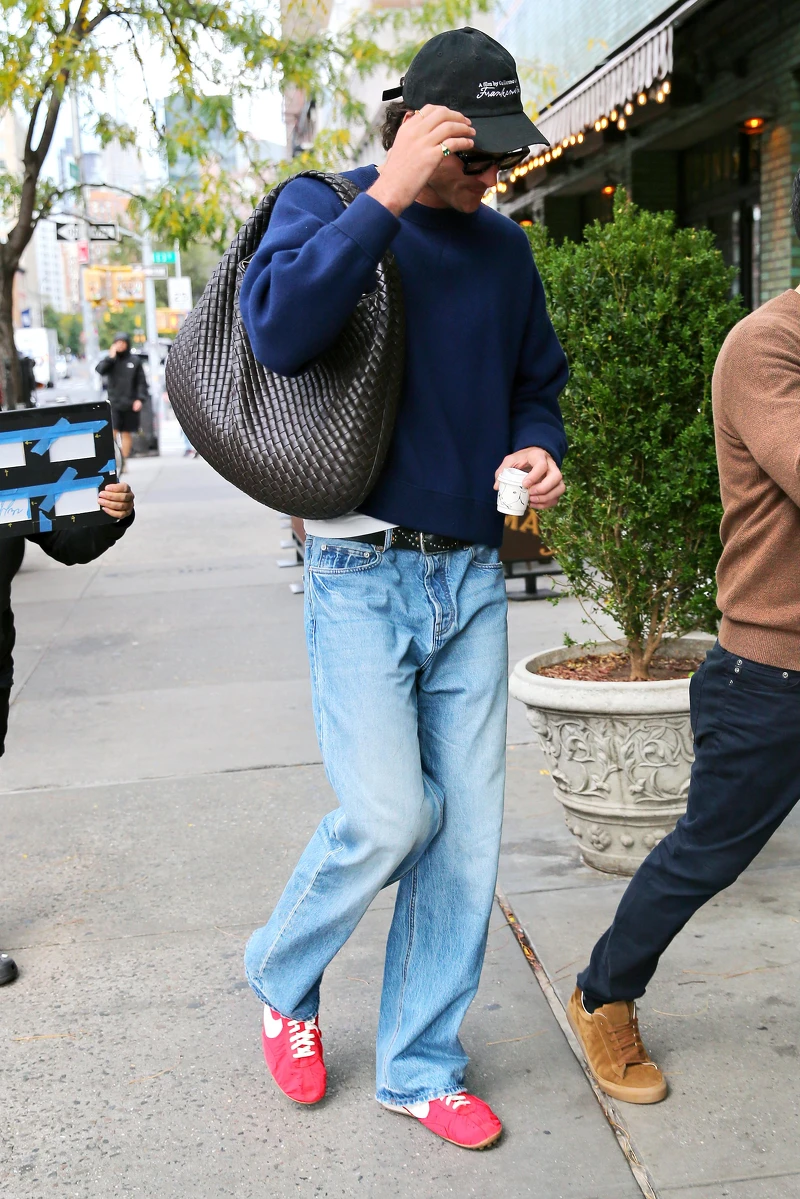 新一代好萊塢男神 Jacob Elordi 的私服造型向來以不經意的比例感見長。他以休閒毛衣搭配牛仔褲，選擇大尺寸 Bottega Veneta 編織包 作為造型主軸，讓工藝感單品在日常穿著中自然成立。棒球帽與紅色 Nike 復古球鞋的加入，替整體造型注入一抹隨性運動氣息，在克制與鬆弛之間取得平衡，展現他一貫低調卻極具辨識度的個人魅力。
