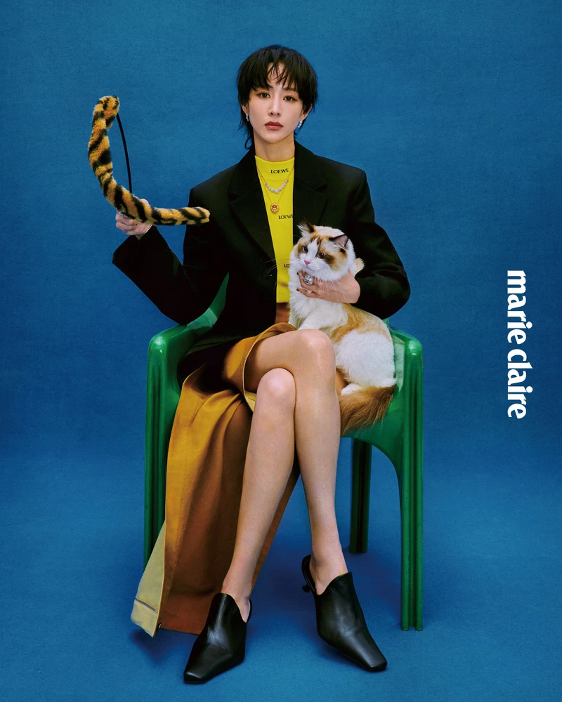 黑色西裝外套、半高領黃色上衣、駝色不對稱裙，all by Loewe； Margherita 瑪格麗特系列18K 黃金黃水晶與鑽石項鍊、Margherita 瑪格麗特系列18K 白金鑽石九朵花卉項鍊、Margherita 瑪格麗特系列18K白金鑽石花卉手環、Margherita 瑪格麗特系列18K 白金鑽石花卉耳環、兩只 Margherita 瑪格麗特系列18K 白金鑽石花卉戒指，Margherita 瑪格麗特系列18K 白金海水藍寶石與鑽石戒指，all by DAMIANI。